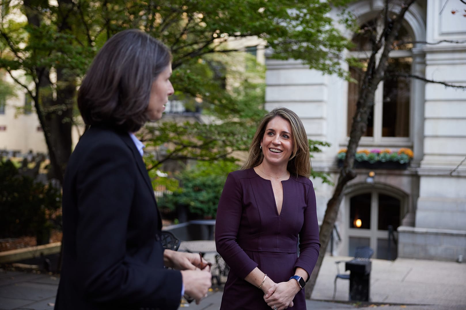 Two women in business attire having a conversation outside of a building